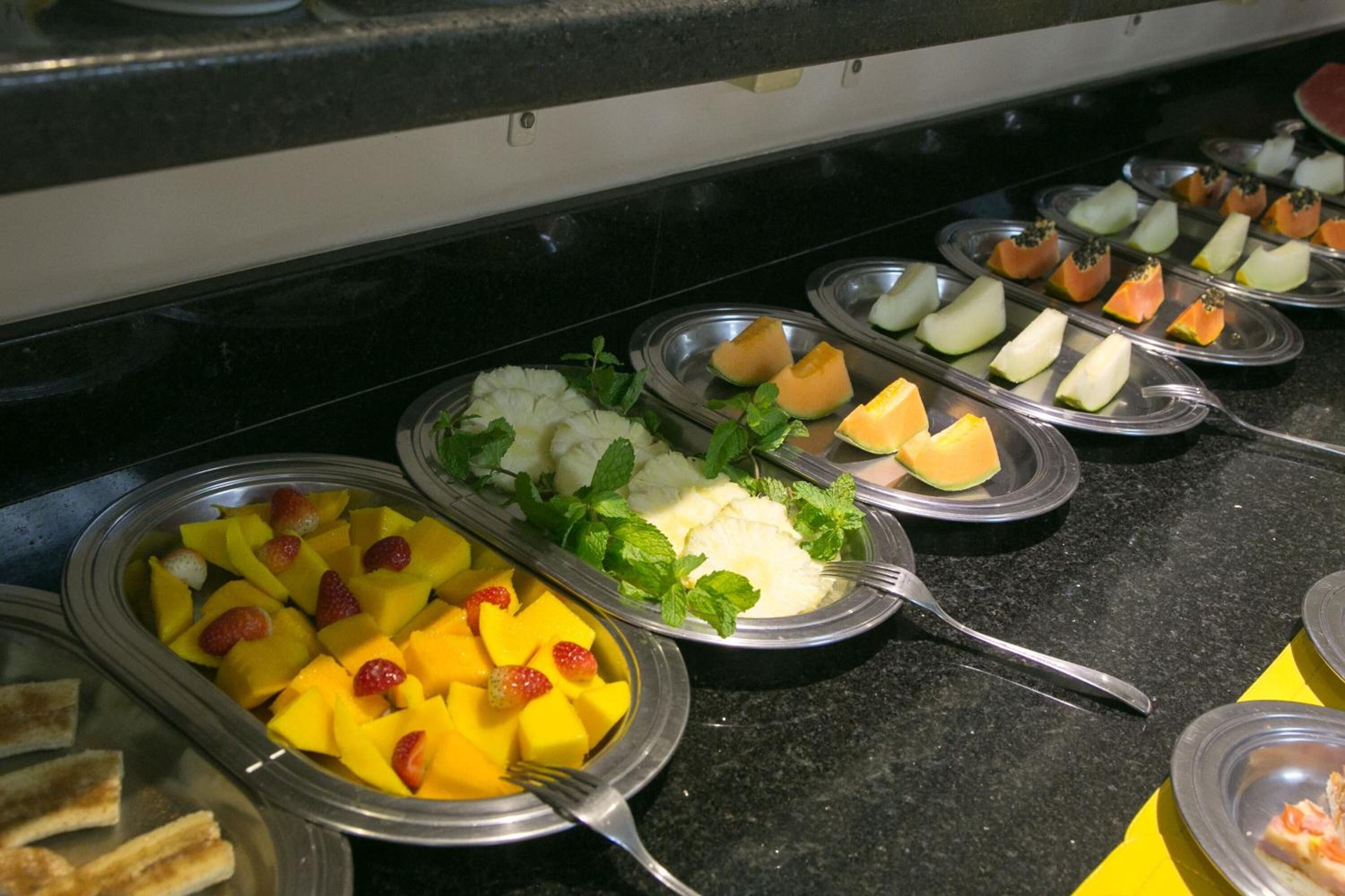 A buffet with various fruits and a slice of cake.