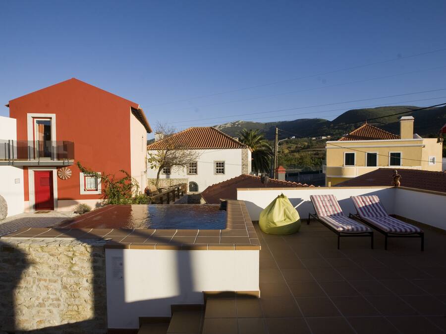 Una terraza en la azotea con piscina, sillas de descanso y vistas de edificios circundantes.