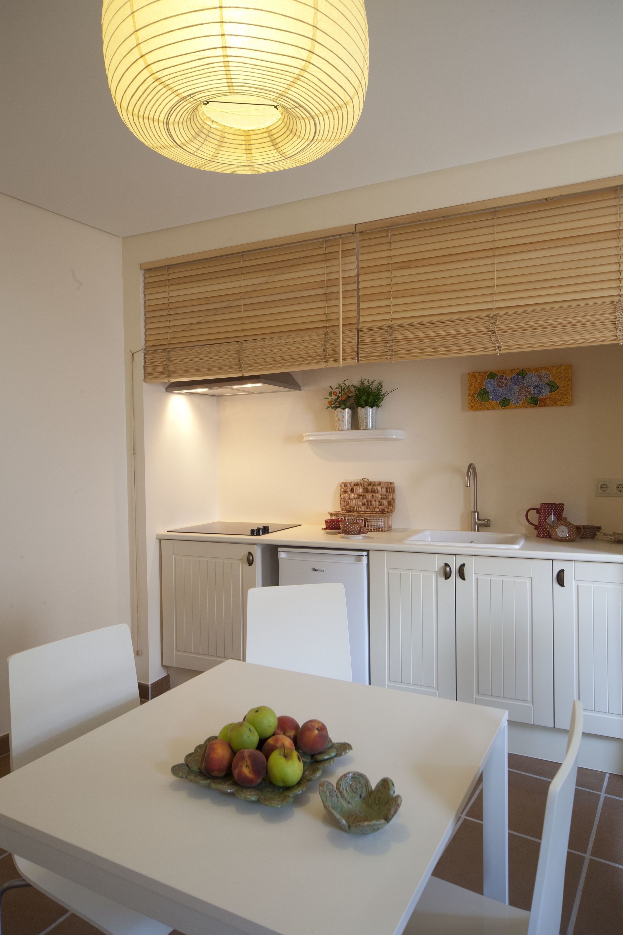A kitchen with white cabinets, a white countertop, and a dining table with a fruit bowl.