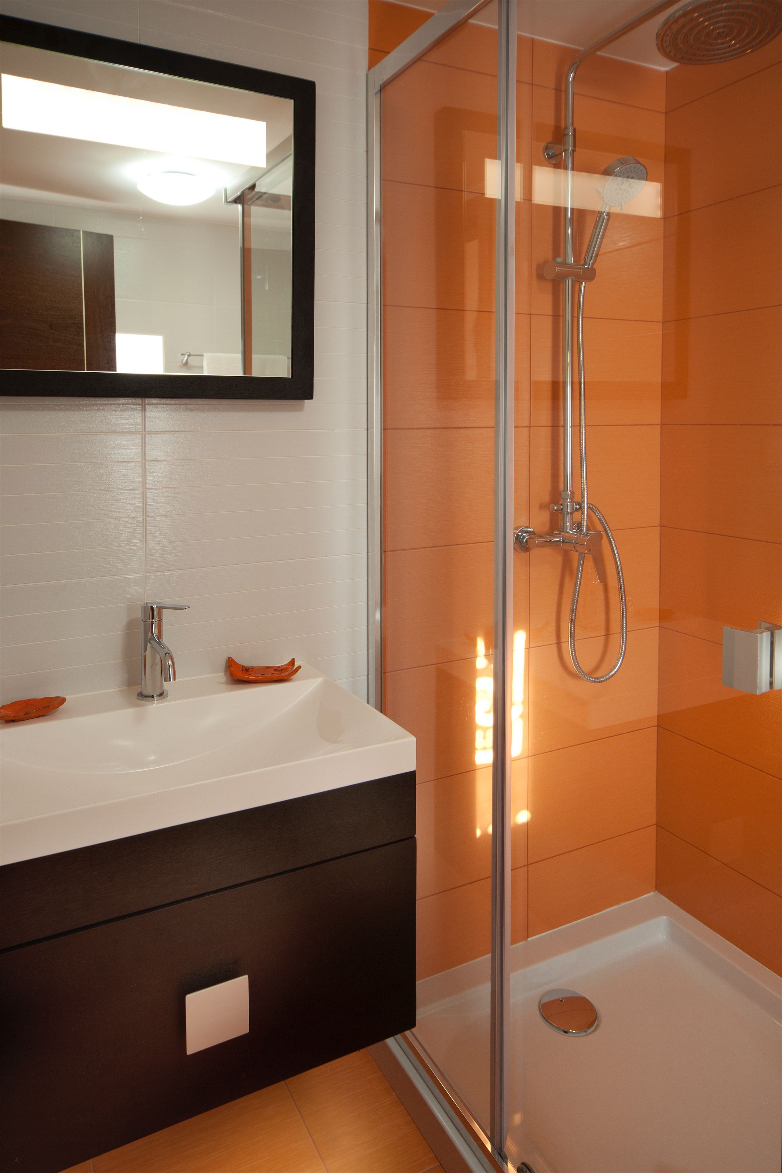 Une salle de bain moderne avec une douche à parois de verre, un lavabo blanc et un meuble-lavabo de couleur foncée.