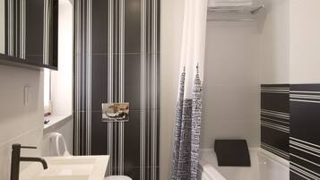 Een moderne badkamer met een wit wastafel, toilet en bad. De wand is gestreept en er is een douchegordijn met een stadsgezicht dessin.