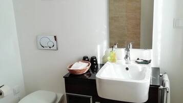 Un baño moderno con un lavabo blanco, tocador negro y un inodoro. Se observa una obra de arte con forma de hoja decorativa en la pared y una pequeña foto enmarcada.