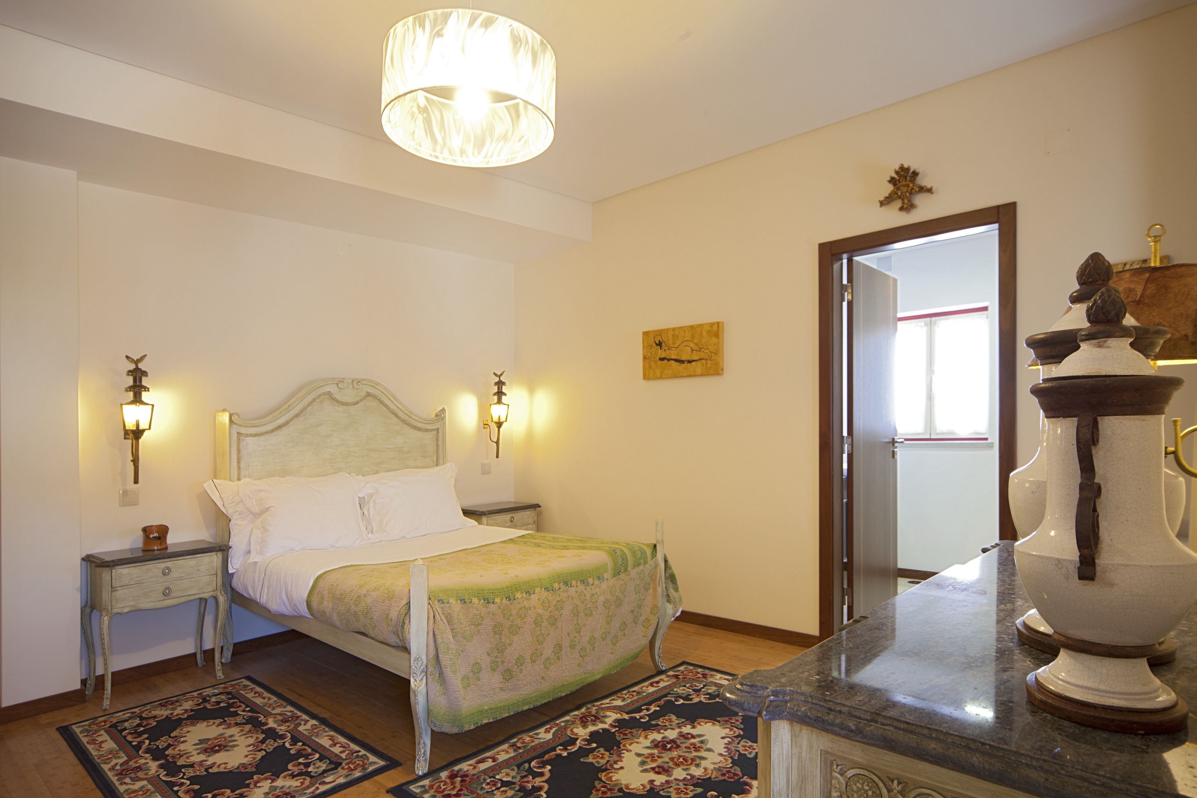 A bedroom with a bed, bedside lamps, a nightstand, a rug, and a decorative vase on the dresser.