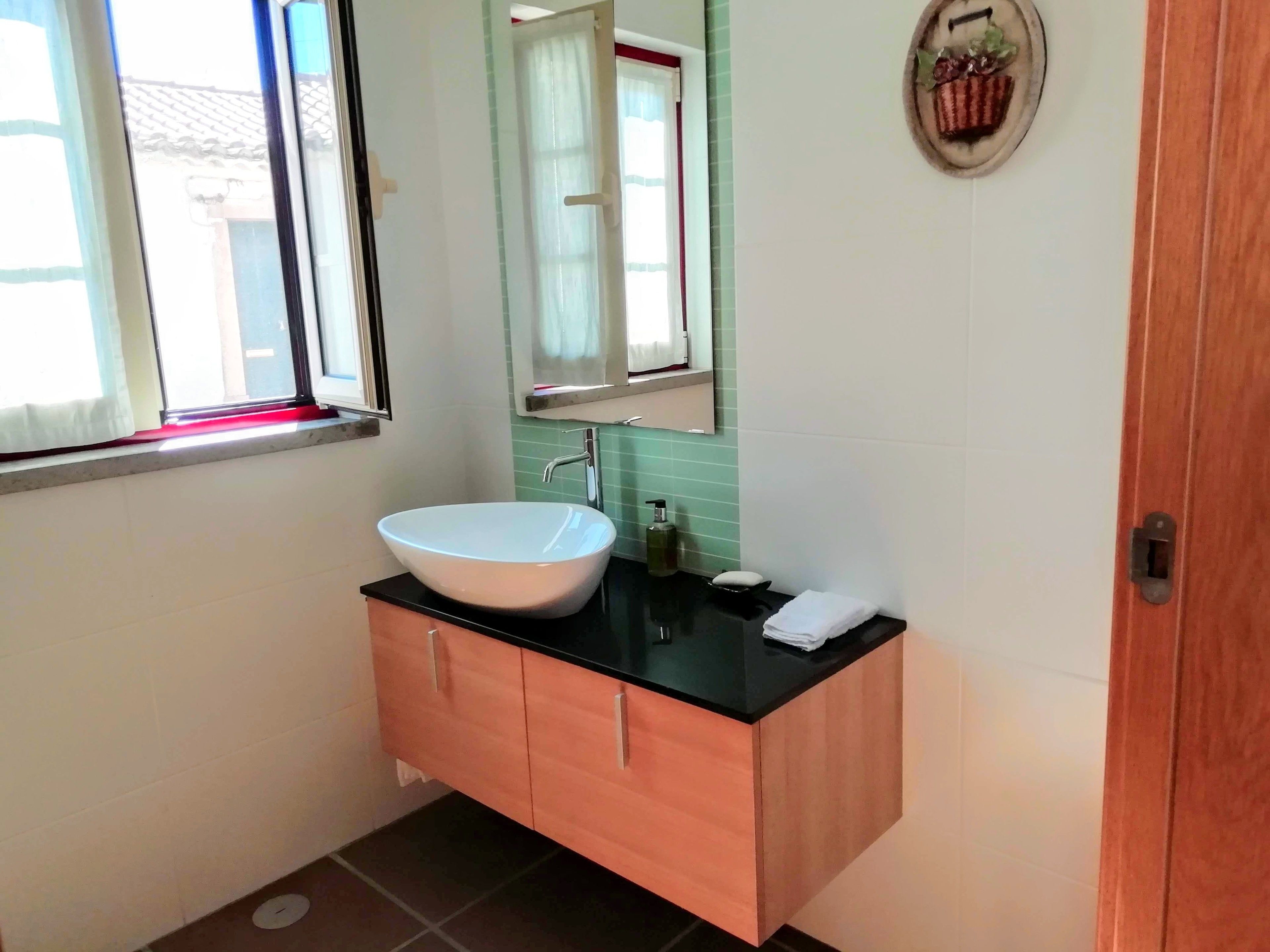 Un baño con un lavabo blanco tipo recipiente, un espejo, un mueble de tocador de madera y una ventana con cortinas.