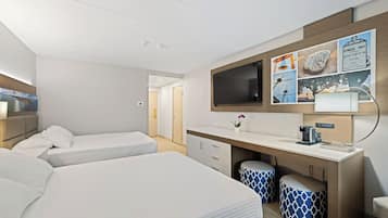 A hotel room with two beds, a desk with a computer, a TV, and a wall with informational posters.