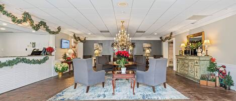A lobby with a chandelier, two armchairs, a coffee table, a reception desk, and a green cabinet with a mirror.