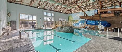 Une piscine intérieure dotée d’un sol en pierre, de poutres en bois et d’une fresque représentant un paysage fluvial.