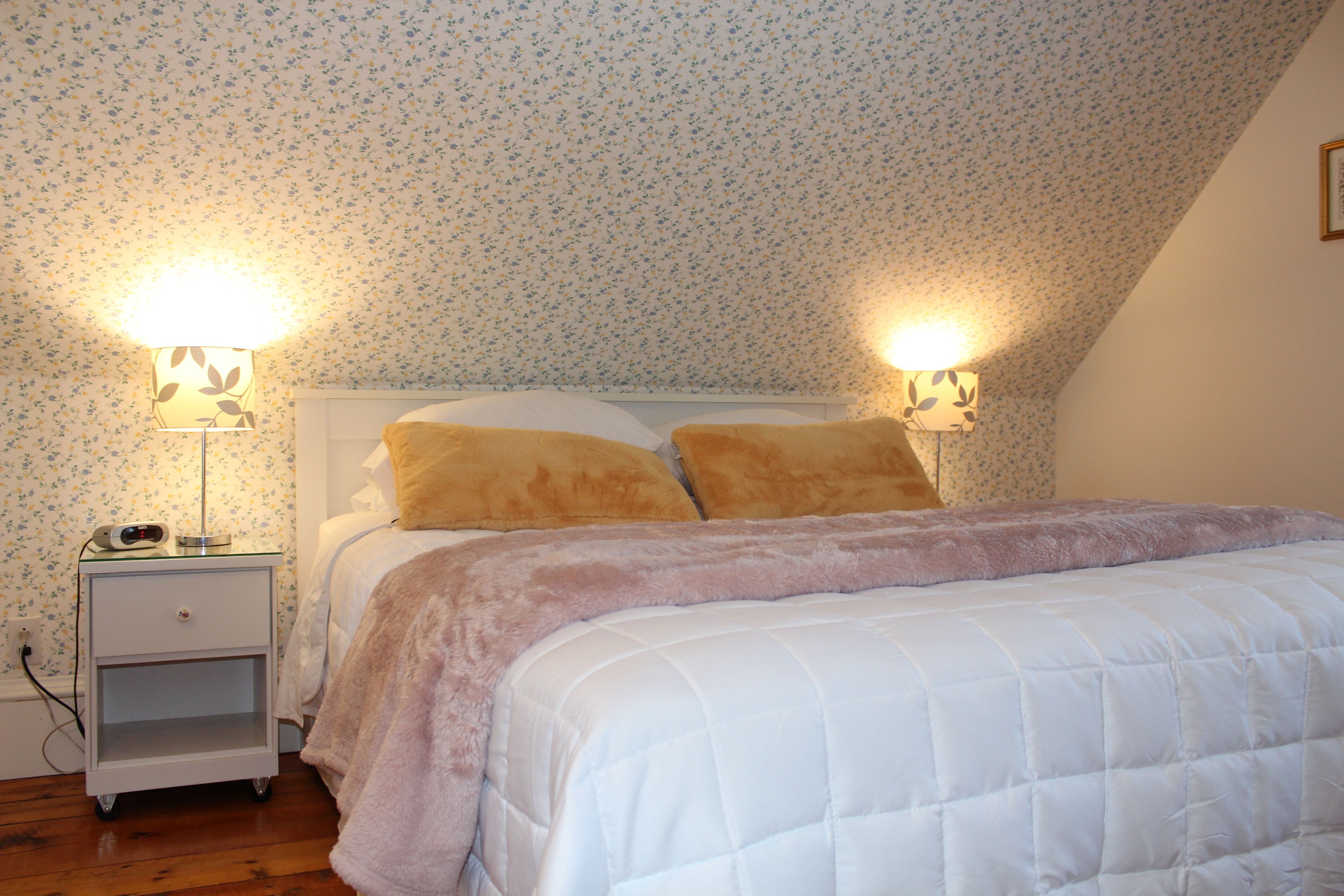 A bedroom with a bed, two bedside lamps, a nightstand, and floral wallpaper.
