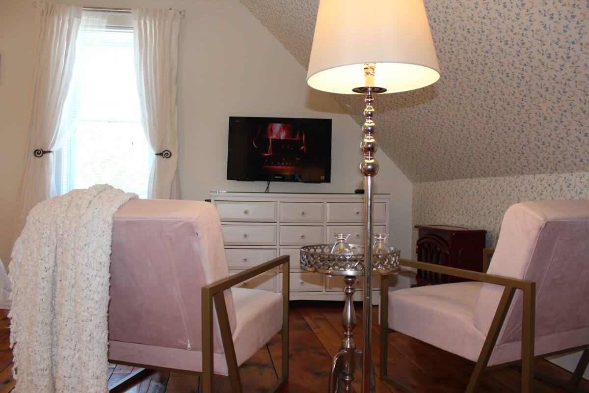 A room with two armchairs, a table with a lamp, a television on the wall, and a patterned wallpaper.