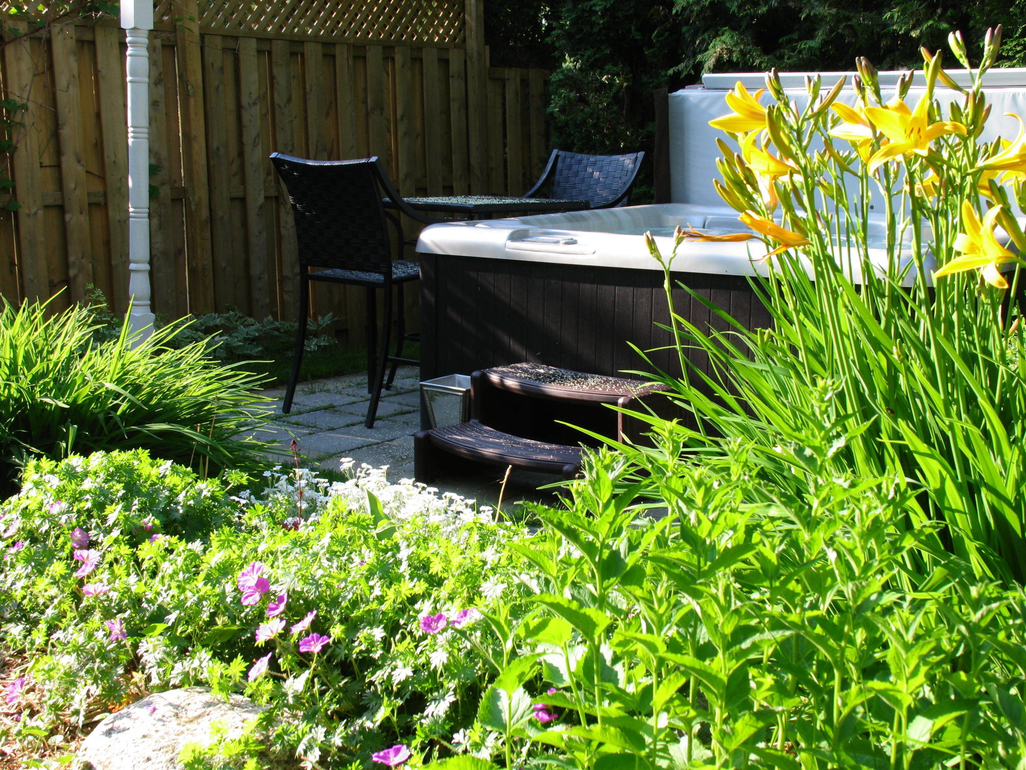 Un patio jardín con un jacuzzi, dos sillas y abundante vegetación.