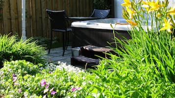 Un patio jardín con un jacuzzi, dos sillas y abundante vegetación.