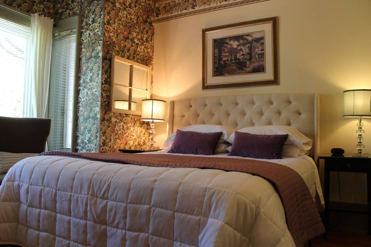 A neatly made bed with a quilted headboard, a bedside table with a lamp, and a framed picture on the wall.