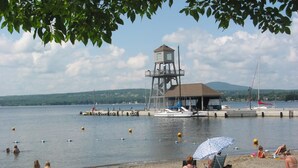 A lakeside setting with a lifeguard tower, boats, and people relaxing on the shore. - Auberge La belle Victorienne (Magog)