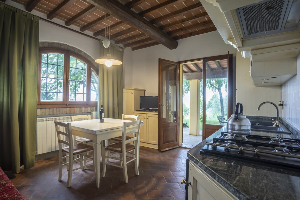 A kitchen with a stove, a dining table with chairs, a television, and a window with curtains.