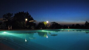 Una piscina al anochecer con sillas de descanso y sombrillas alrededor.