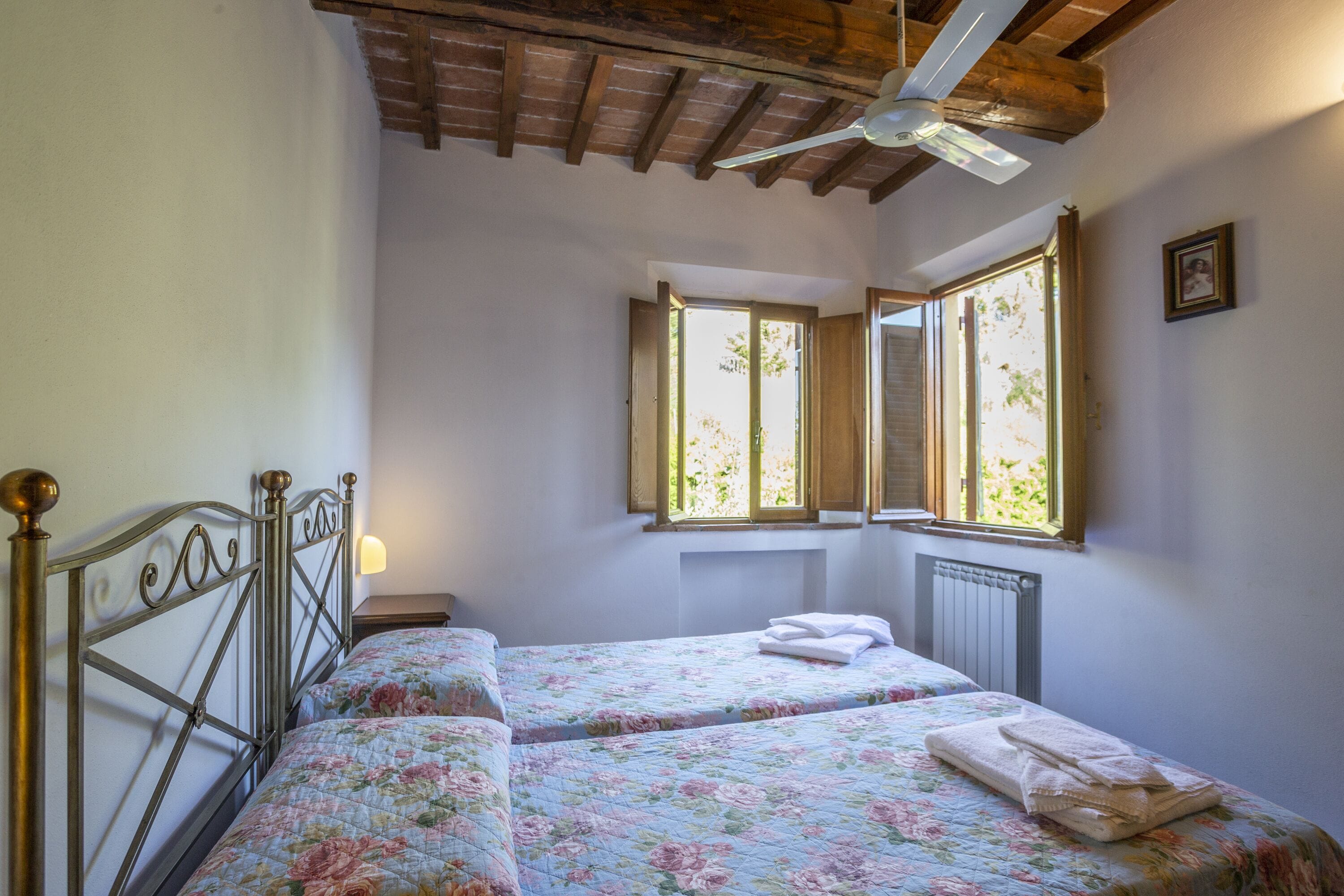 A bedroom with two beds, wooden beams on the ceiling, a window with a view, and a radiator.