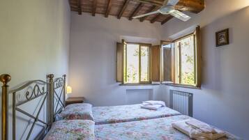 A bedroom with two beds, wooden beams on the ceiling, a window with a view, and a radiator.