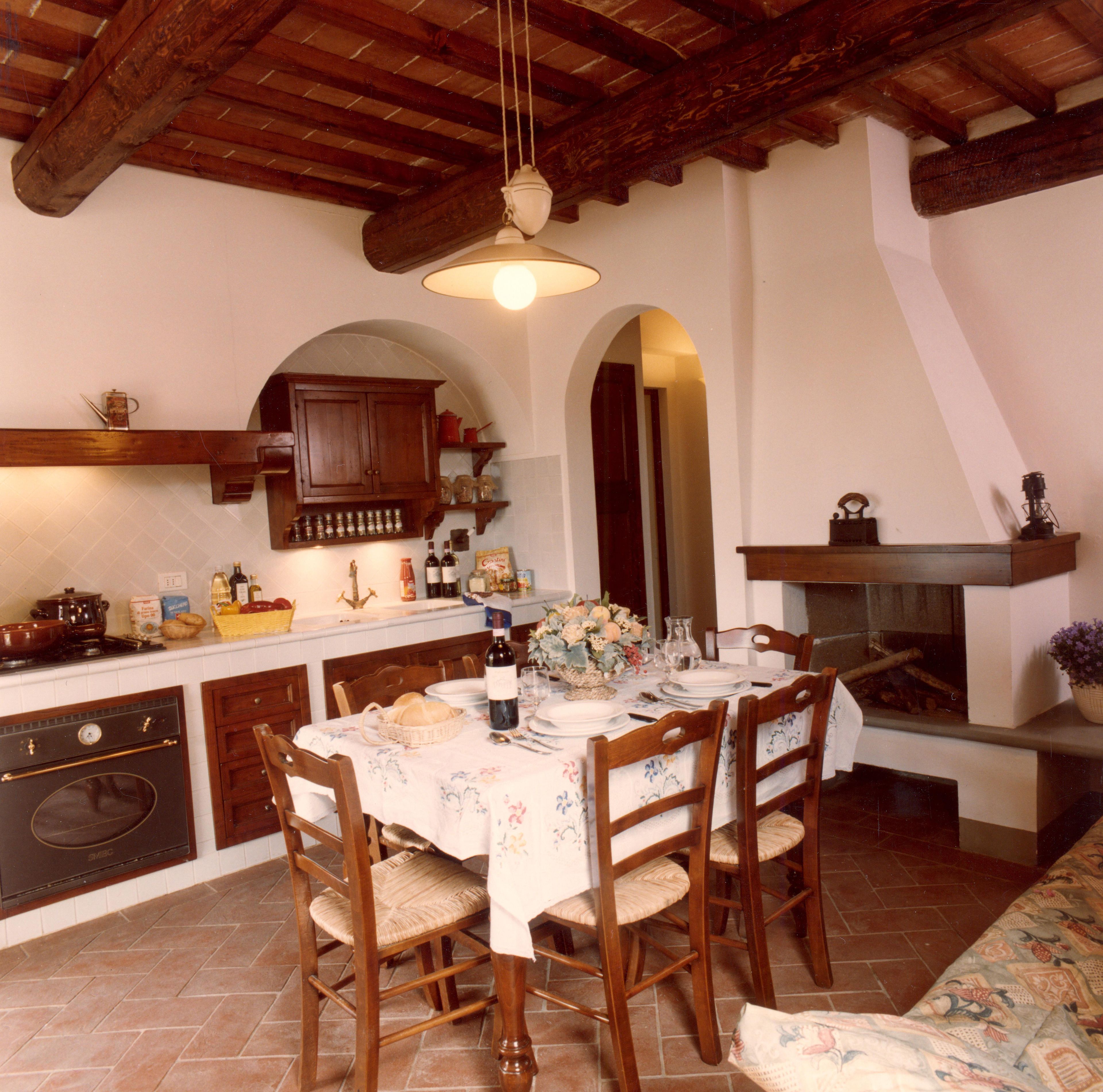 A rustic kitchen with wooden beams, a dining table set for four, and a fireplace.