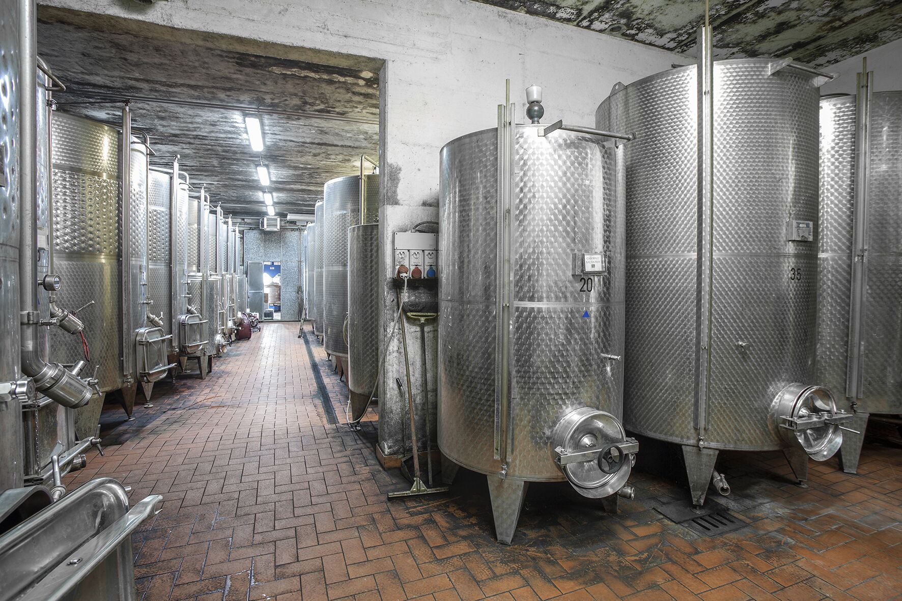 Sèrie de dipòsits d'acero inoxidable per a la fermentació en una cervateria, amb un sòl de maó i un sostre de formigó.