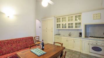 Cocina compacta con armarios blancos, una mesa de comedor y un sofá rojo con estampado.