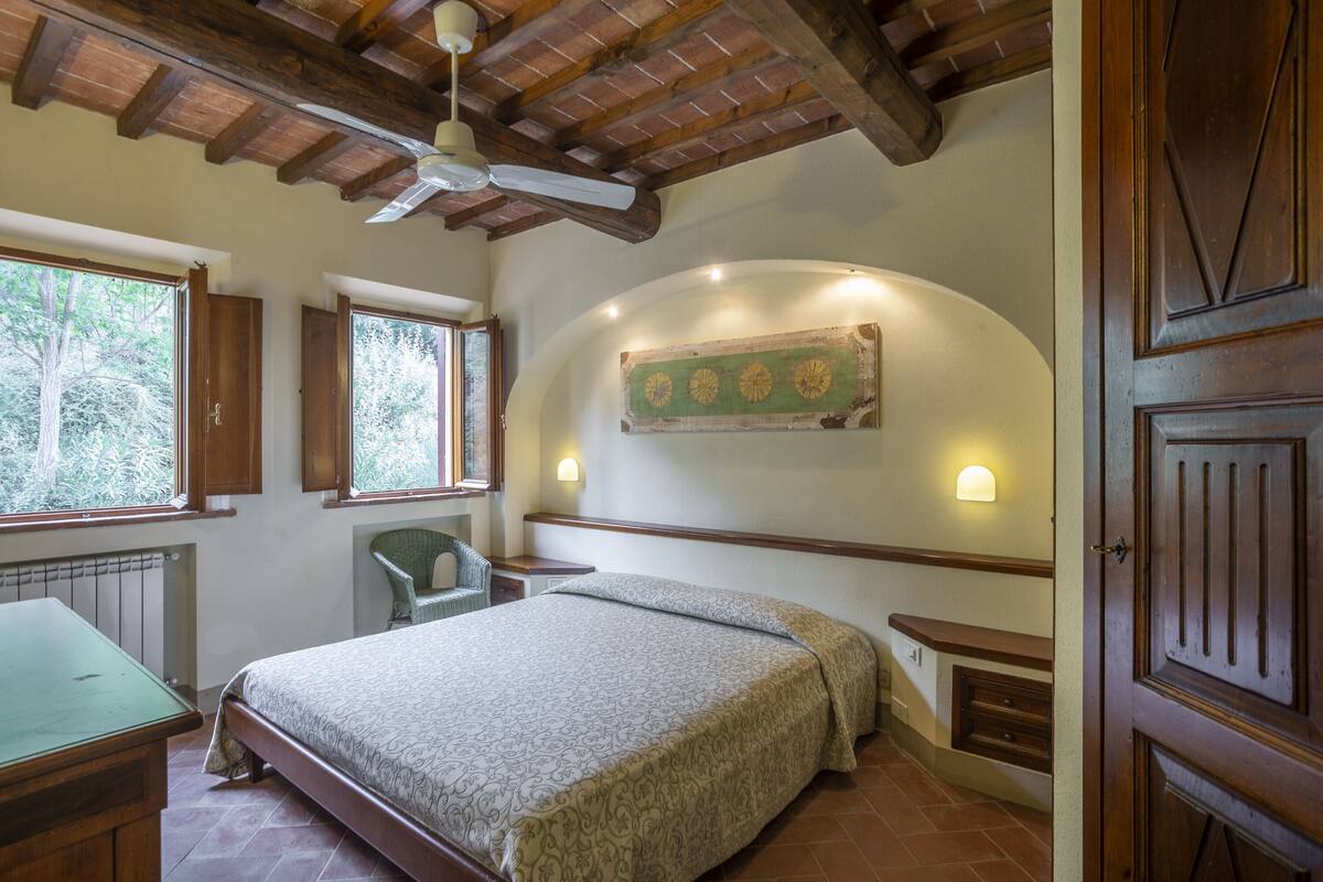 A bedroom with a bed, a chair, a desk, a radiator, and a door.