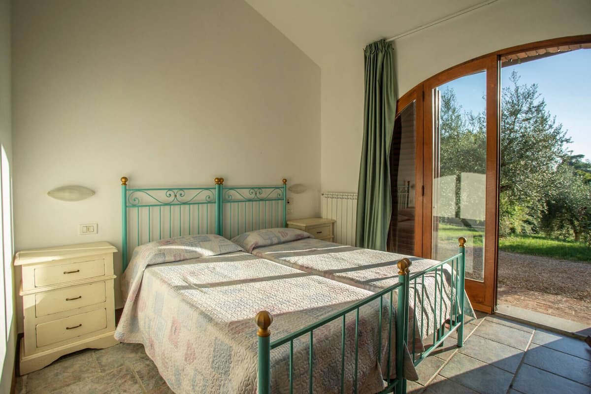 A bedroom with a bed, bedside tables, a dresser, and a sliding glass door leading to a garden.