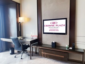 A hotel room with a desk, chair, and a television mounted on the wall displaying the Crowne Plaza logo.