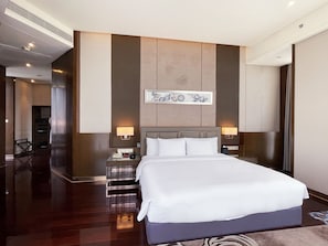 Una habitación de hotel moderna con una cama grande, dos mesitas de noche, una lámpara de pie y una obra de arte en la pared, además de un pasillo que conduce a una escalera.