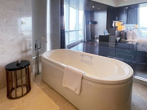 Un baño moderno con una bañera independiente, un taburete redondo pequeño y una zona de ducha con paredes de vidrio.