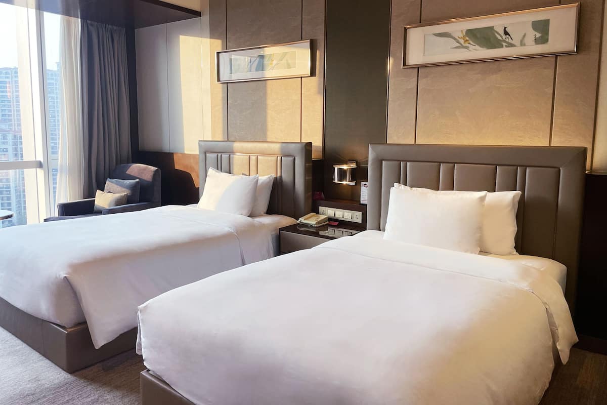 A hotel room with two beds, a nightstand, a lamp, and a window with curtains.