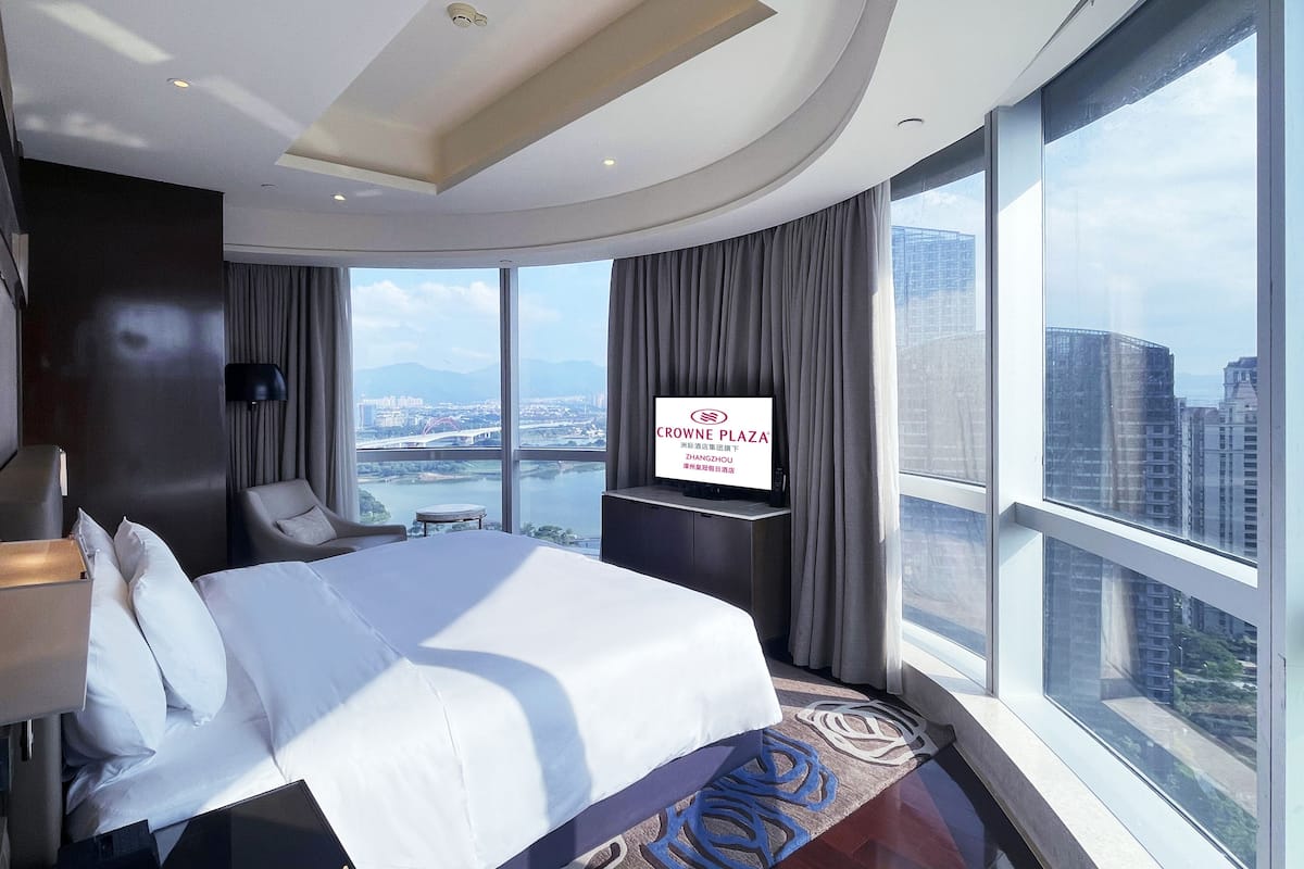 A modern hotel room with a large bed, a TV, a desk, and a view of the city.