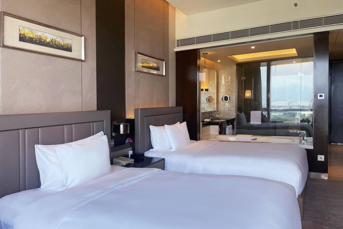 Een hotelkamer met twee bedden, een badkamer met een grote spiegel en uitzicht op de stad.