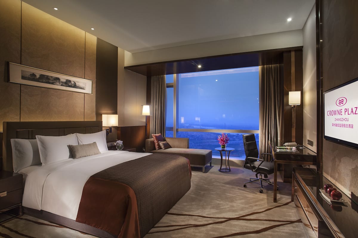 Een hotelkamer met een groot bed, een bureau, een stoel en een televisiescherm waarop de naam van het hotel staat.