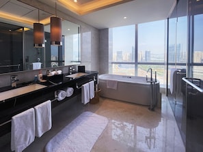 A modern bathroom with a large mirror, two sinks, a bathtub, and a view of the city through large windows.