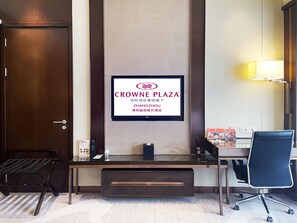 A hotel room with a desk, chair, and a wall-mounted television displaying the Crowne Plaza logo.