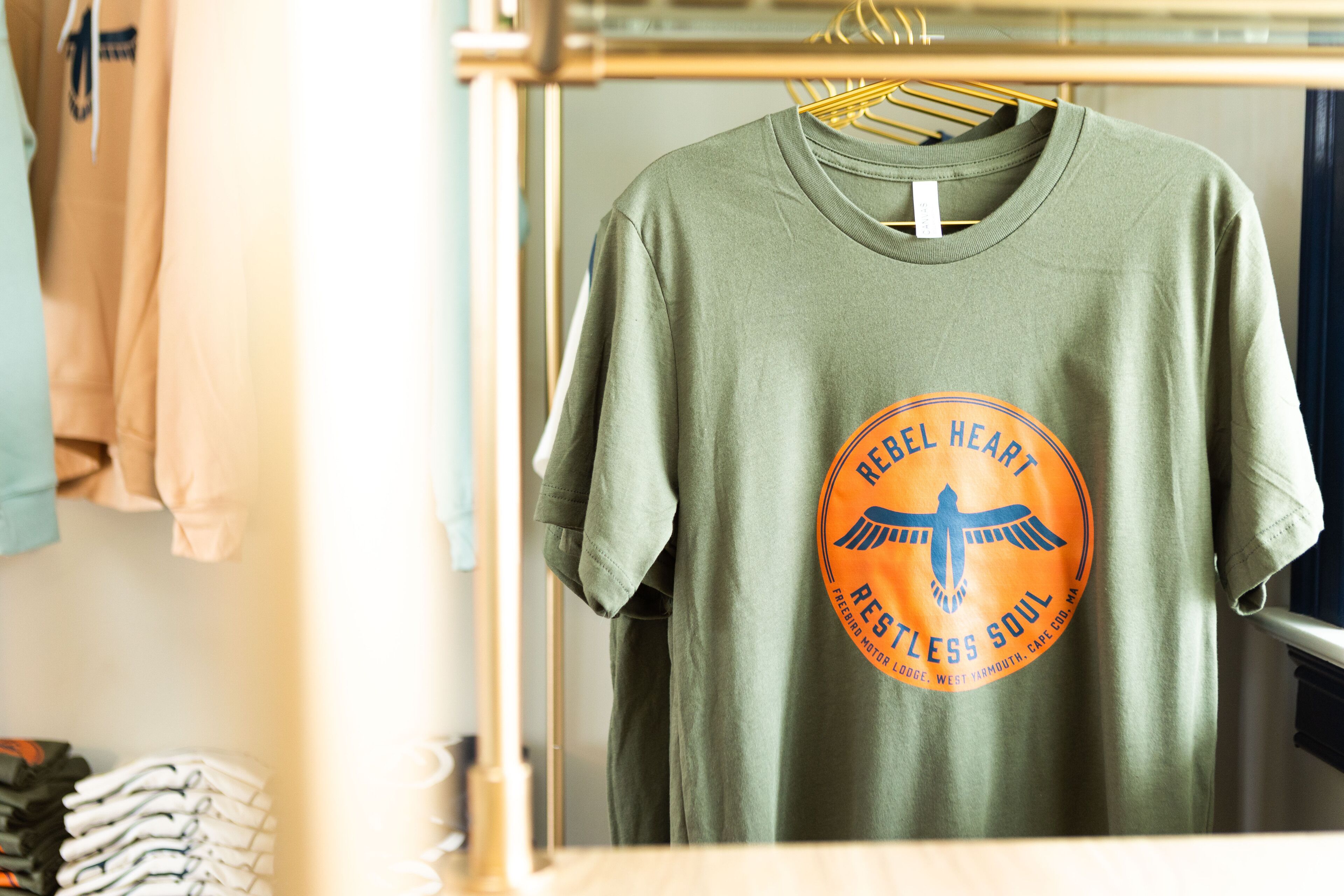 A green t-shirt with a circular logo hanging on a rack.