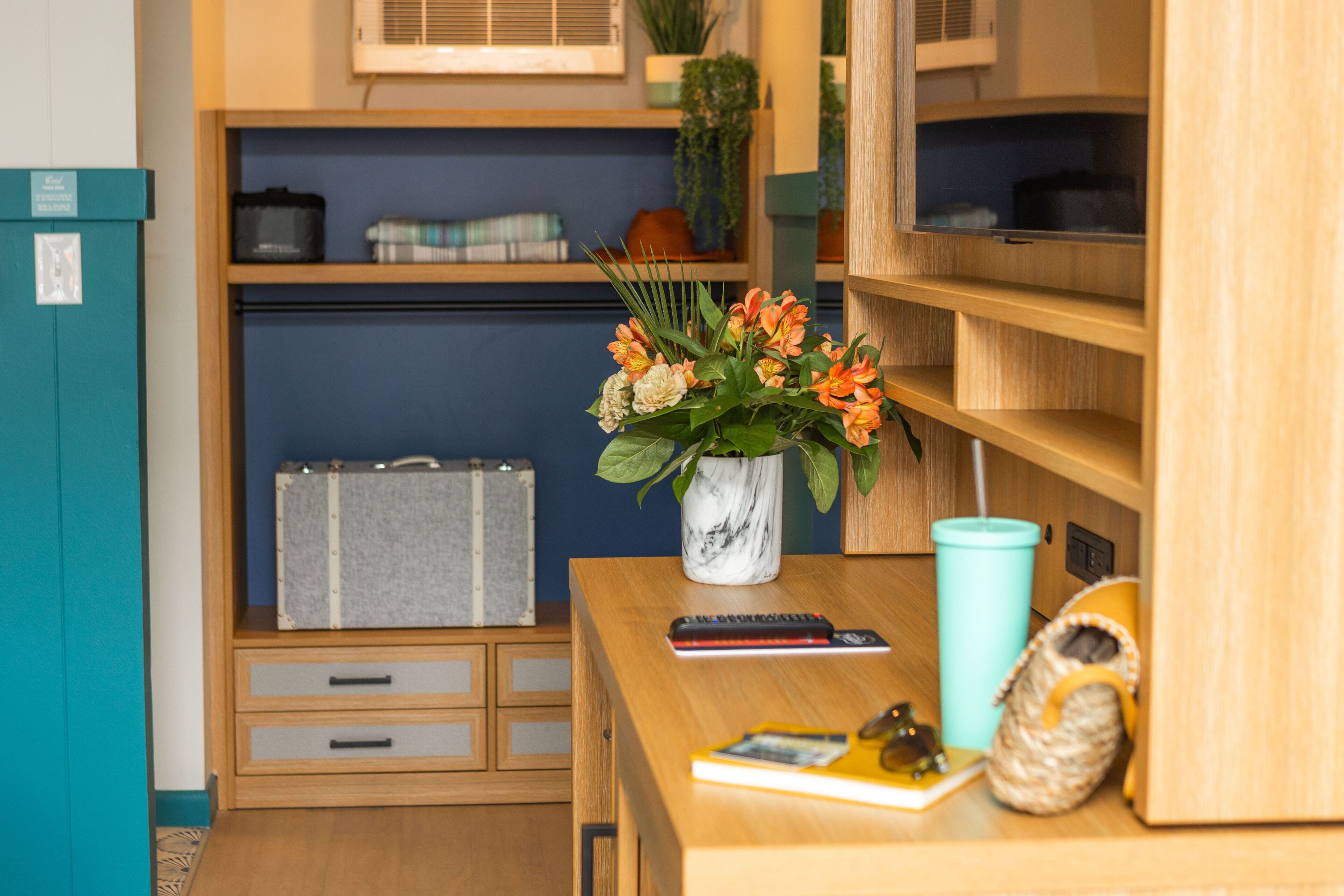 A neatly organized room with a wooden desk, a vase with flowers, a remote control, a book, and a small decorative item.