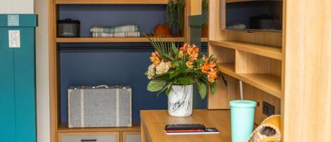 A neatly organized room with a wooden desk, a vase with flowers, a remote control, a book, and a small decorative item.
