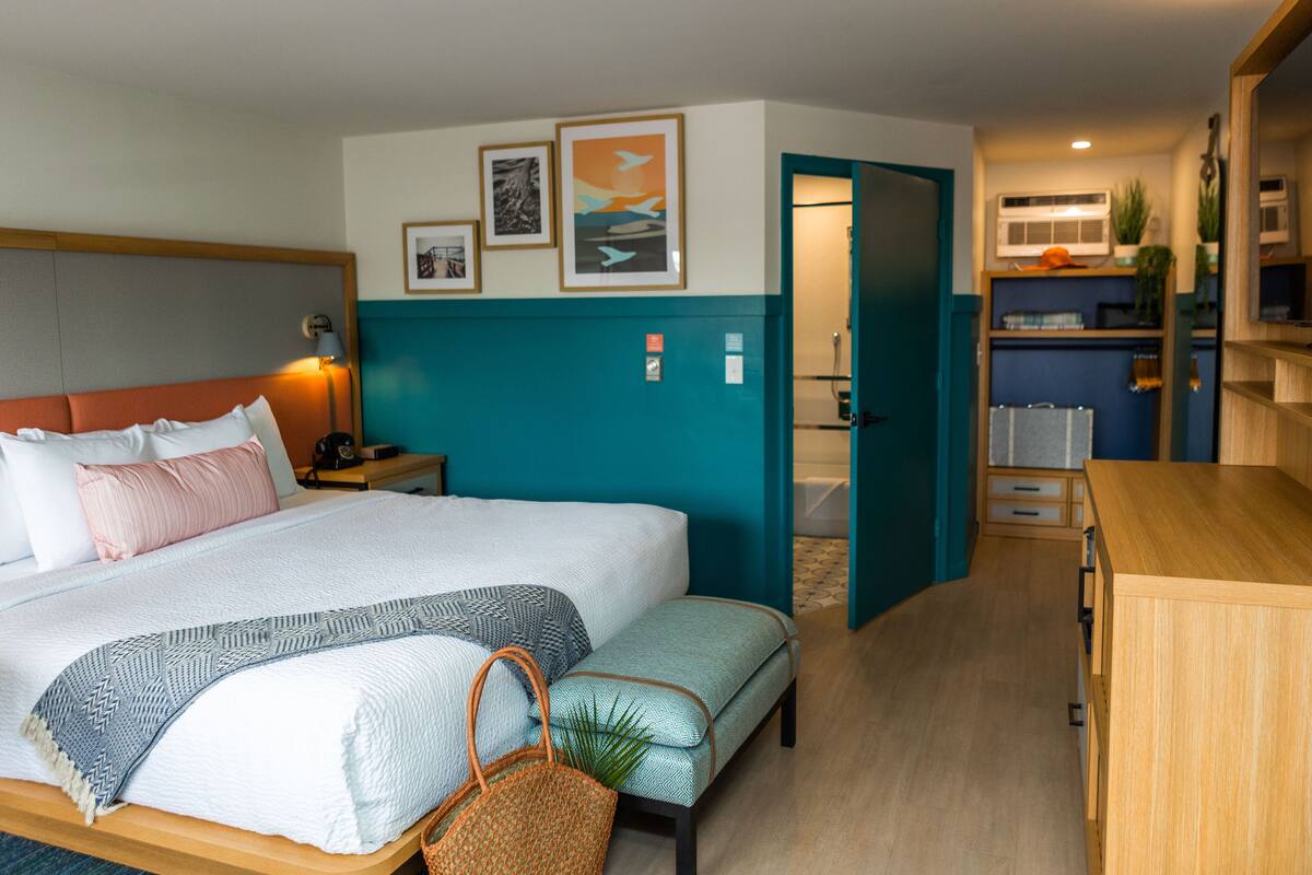 Quarto de hotel com cama, mesa de cabeceira, luminária e obra de arte na parede.
