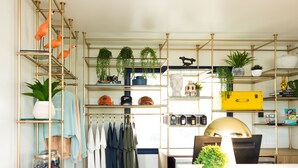 A room with a wooden desk, shelves with plants, and hanging clothes. - Freebird Motor Lodge by Reverie Boutique Collection (West Yarmouth)