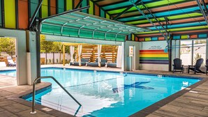 An indoor swimming pool with a tiled floor, a diving board, and a covered seating area with chairs. - Freebird Motor Lodge by Reverie Boutique Collection (West Yarmouth)