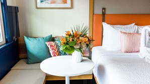 A hotel room with a bed, a round white table with a vase of flowers, and a seating area with cushions. - Freebird Motor Lodge by Reverie Boutique Collection (West Yarmouth)