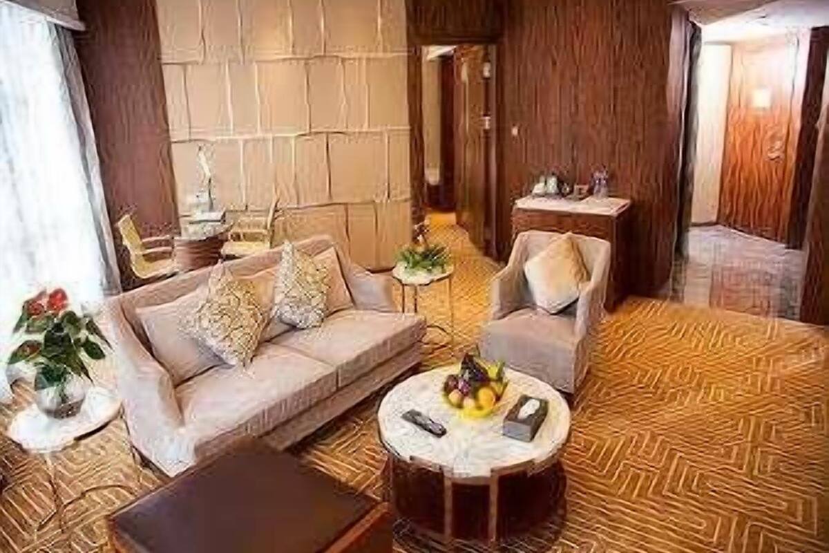 Een moderne hotelkamer met een bank, fauteuil en een klein rond tafeltje met fruit.