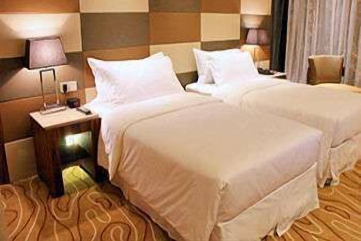 Een hotelkamer met twee bedden, een nachtkastje met een lamp en een kamerbreed tapijt met een patroon.