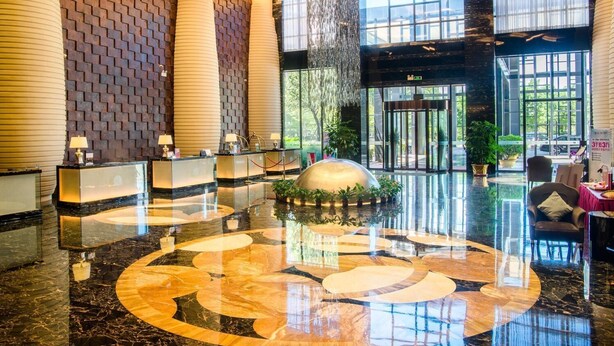 Een moderne hotellobby met een receptiebalie, een fontein in het midden en een glazen lift.