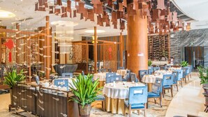 Een modern restaurant met ronde tafels, blauwe stoelen en hangende houten decoraties.