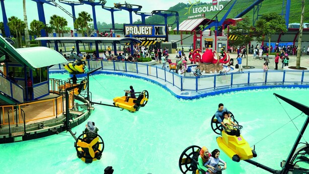 Un paseo acuático con botes amarillos, una zona temática de LEGO y una montaña rusa al fondo.