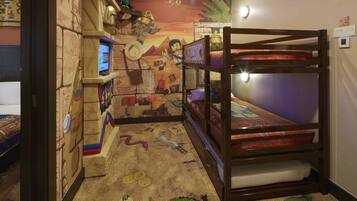 Una habitació infantil amb un llit superposat, una zona de jocs amb una pantalla i un mural a la paret.
