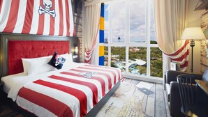 Habitación de hotel con una cama grande, vistas a un paisaje urbano y una ventana con cortinas.