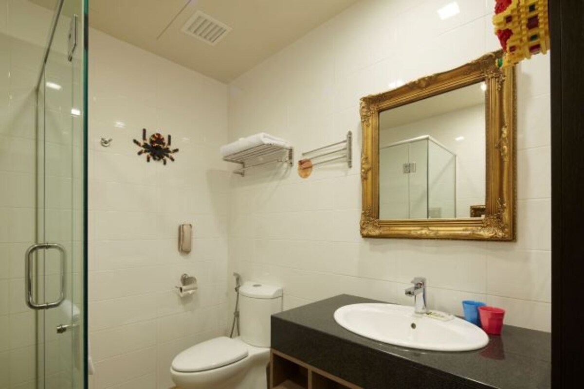 Un baño con cabina de ducha de vidrio, inodoro blanco, lavamanos con espejo de marco dorado y toallero.